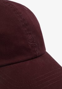 Gorra de béisbol color marrón oscuro hecha de tela texturada, con un detalle de calavera bordado. Su forma incluye una corona redondeada y un visera rígida.