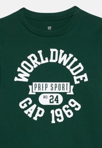 Tamnozeleni dječji majica s bijelim natpisom "WORLDWIDE GAP 1969" i "PREP SPORT br. 24" u središtu sprijeda.