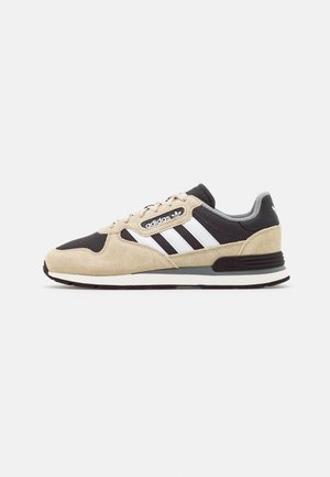 Adidas-tossut, joissa on beige mokka- ja musta verkko-yläosa, valkoinen kolmiraidallinen yksityiskohta sekä harmaat korostukset kantapäässä ja pohjassa.