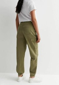 Olivengrønne cargo bukser med elastisk talje, manchetter ved anklerne og flere lommer. Bæres med en hvid T-shirt og hvide sneakers.