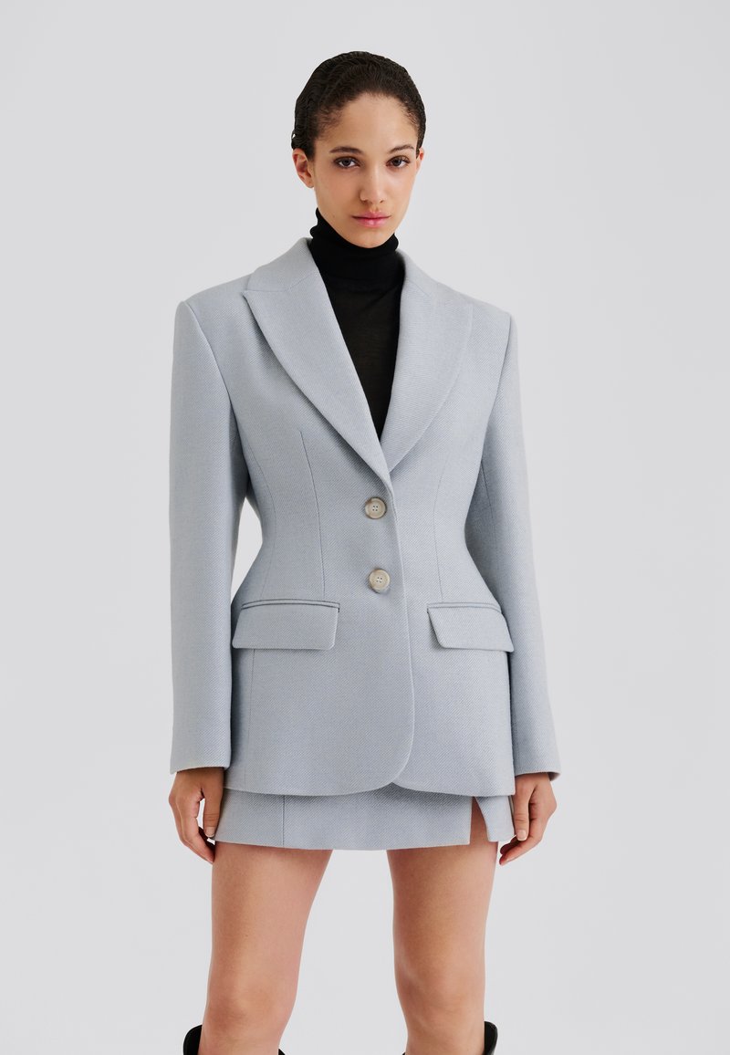 Blazer bleu clair cintré avec larges revers, deux boutons et deux poches avant, associé à une mini-jupe, le tout en tissu texturé.