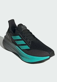 Scarpa sportiva nera con accenti turchesi. Presenta una parte superiore testurizzata, tre strisce diagonali e una suola spessa e ammortizzata.