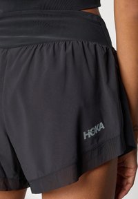 Black running shorts made of lightweight fabric with a gathered elastic waistband and a subtle HOKA logo on the lower side.