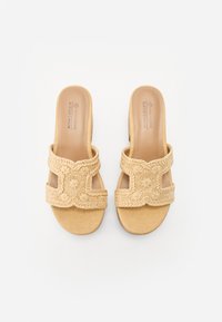 Braune gewebte Schlüpfsandalen mit einem breiten Riemen mit einem Kreuzdesign und strukturierter Oberfläche, auf einer glatten Fußbett und flachen Sohle.