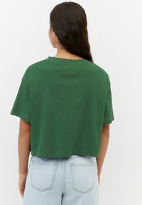 T-shirt verde a maniche corte e cropped, realizzata in cotone morbido, con una vestibilità comoda e scollo rotondo. Indossata con jeans azzurri chiari.