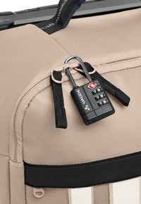 Dettaglio di una borsa in tessuto beige con una cerniera combinata dotata di un lucchetto combinato nero, e una tracolla nera con strisce beige.