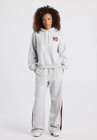Hellegraue Hoodie- und Hosenkombination mit einem burgunderfarbenen "89" Druck, entspannter Passform, Kapuze mit Kordelzug und seitlichem Akzent in Dunkelrot.