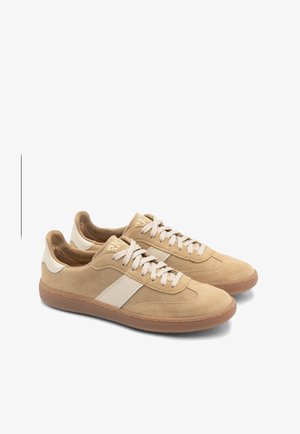 Šviesiai rudos nubuko sportbačiai su kreminiais akcentais, turintys tekstūruotą šoninį panelį, plokščias raišteles ir guminius padus.