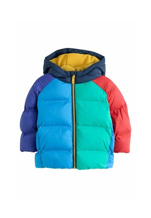 Jeune garçon portant une doudoune colorée avec des sections bleues, vertes, rouges et violettes, un jean bleu et des baskets blanches, debout et regardant vers la droite.