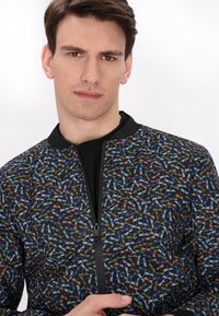 Giacca bomber nera con un motivo floreale multicolore, chiusura con zip sul davanti e collo a costine. Tessuto leggero con una texture liscia.