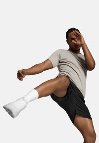 Sportlik riietus, mis sisaldab heledat halli lühikeste varrukatega särki ja musti lühikesi pükse, koos valgete pahkluu sokkide ja valgete kingadega, aktiivses poosis.