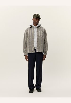 Gray button-up shirt with vertical stripes, gray hoodie underneath, black pants, and a dark green baseball cap. Smooth fabric and casual fit.