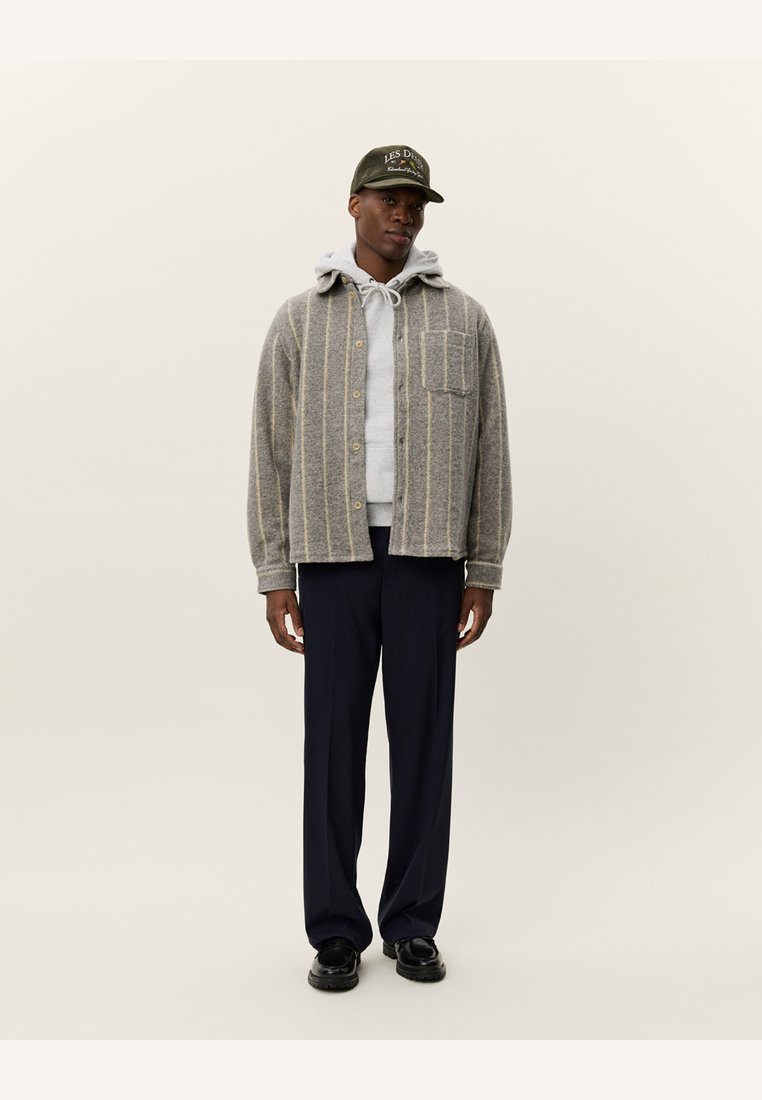 Gray button-up shirt with vertical stripes, gray hoodie underneath, black pants, and a dark green baseball cap. Smooth fabric and casual fit.