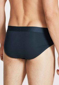 Schwarze, glatte Stoffunterhosen mit einem stützenden Bund, taillierter Passform und minimaler Bedeckung, die eine einheitliche Farbe und eine elegante Textur präsentieren.