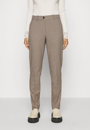 Femme portant un pantalon ajusté à carreaux beige et noir avec taille à boutons, associé à des mocassins crème et à un pull blanc ajusté.