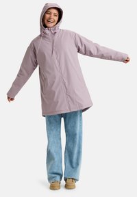 Chaqueta impermeable de color púrpura claro con capucha, que cuenta con un cierre frontal, cordones elásticos y bolsillos laterales, combinada con jeans de color azul claro.