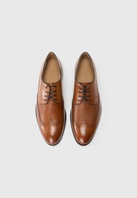 Zapatos de vestir de cuero marrón con detalles perforados, diseño de punta de ala y cordones negros. Acabado suave con puntera pulida y lateral texturizado.