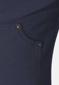 Marineblaue Sweatshirtstoffe mit strukturierter Oberfläche. Verfügt über eine knopfförmige Tasche mit abgerundeter Form und sichtbaren Nähdetails.