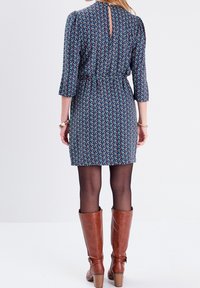 Dunkelblares Kleid mit Blumenmuster, tailliert, mit Dreiviertelärmeln und einem Ausschnitt im Rücken. Dazu braune kniehohe Stiefel.