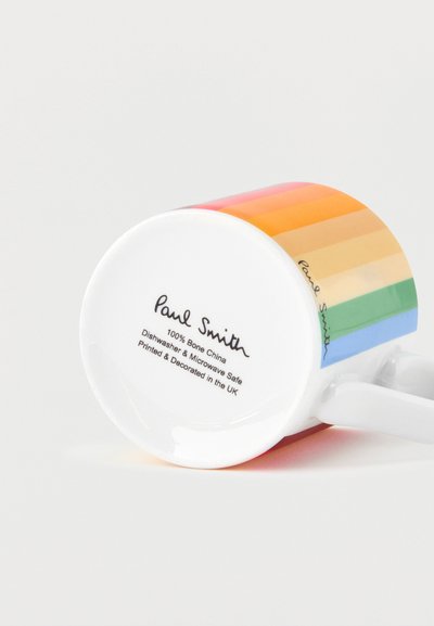 Mug en céramique blanc avec des rayures arc-en-ciel horizontales et le logo Paul Smith, posé sur le côté avec un texte indiquant qu'il est compatible lave-vaisselle et micro-ondes.