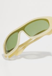Sport sunglasses with a pale yellow plastic frame and green tinted lenses, featuring a sleek, aerodynamic design and curved temples.