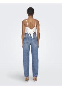 Top blanco con tirantes finos atado por la espalda, combinado con jeans de mezclilla azul de cintura alta con un ajuste holgado y cinco bolsillos. Texturas suaves a la vista.
