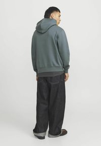 Gray hoodie with a large hood, ribbed cuffs, and hem. Paired with loose-fitting dark denim jeans and brown shoes.