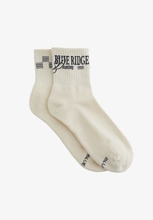 Coppia di calzini crema a coste con la scritta "BLUE RIDGE denim" in nero vicino al bordo superiore e "BLUE" sull'area delle dita.