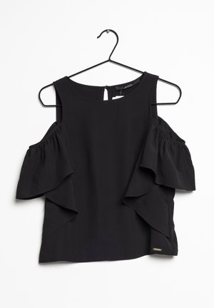 Blouse noire épaules dénudées avec manches à volants suspendue sur un cintre en fil noir sur fond blanc.