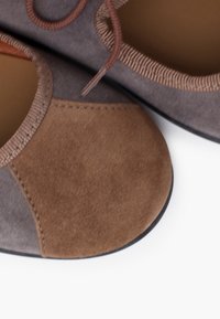 Flache Schuhe in Grautönen und Braun. Hergestellt aus weichem Wildleder, mit kontrastierendem Paneldesign und elastischen Akzenten entlang der Kanten.