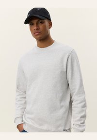 Sudadera gris claro hecha de una tela suave, con cuello redondo, puños acanalados y un pequeño detalle de logo en el dobladillo.