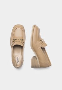 Beige leren instapschoenen met een vierkante neus en een decoratieve gouden kettingaccent. Lage blokhak met horizontale ribbels voor grip.