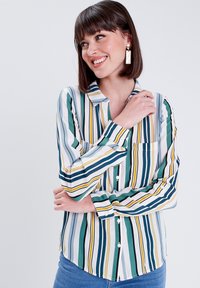 Chemise rayée en blanc, vert, marine et jaune. Présente un devant à boutons, un col et une poche poitrine unique avec des manches longues.