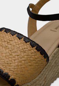 Πλεκτό σανδάλι εσπαντρίγια από άχυρο με μαύρη πλεκτή λωρίδα, ταμπά βάση και μαύρο λουρί. Υφή επιφάνειας και στρογγυλεμένο σχεδιασμό μύτης.