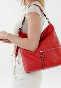 Sac hobo en cuir rouge au design souple, avec une poche zippée à l'avant et un détail de sangle réglable. Texture lisse et couleur audacieuse.