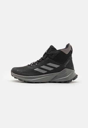 Czarne buty trekkingowe z teksturowaną cholewą, materiałem Gore-Tex, szarymi paskami akcentującymi, wzmocnioną osłoną palców i solidną podeszwą zapewniającą przyczepność.
