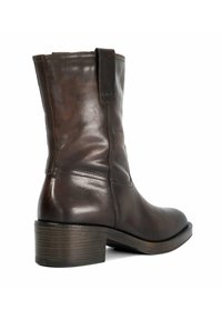 Brown leather ankle boot with a smooth finish, stacked heel, and a pull tab. Features minimal stitching and a rounded toe design.