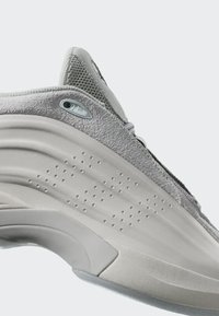 Krupni plan pete svijetlosivog tenisica s teksturiranim gornjim dijelom, perforiranom srednjom đonom i zakrivljenim dizajnom potplata na bijeloj pozadini.