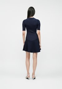 Vestido ribeteado en azul marino con un corsé ajustado y falda acampanada. Mangas cortas, tela texturizada y detalles en la costura trasera. Se lleva con zapatos de tacón grises.