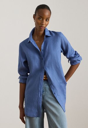 Ανοιχτό μπλε λινό πουκάμισο με κουμπιά, άνετη γραμμή, μανίκια γυρισμένα και κλασικό γιακά, συνδυασμένο με ψηλόμεσα τζιν.