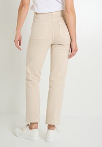 Pantalons beige ajustés avec une taille haute et des poches arrière, conçus dans un tissu lisse. Associés à des baskets blanches, affichant un ourlet court.