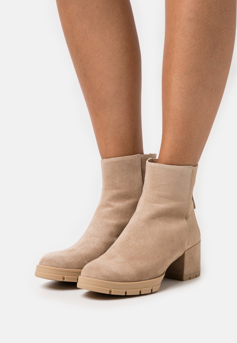 Kengät, joissa on beige mokka pinnalta, sileä rakenne, pyöreä kärki ja lohkare-korko. Takana on vetoketju ja kumipohja, jossa on urat.