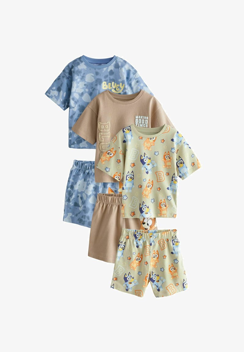 Tre sæt med børnetoppe med korte ærmer og shorts i blå batik, beige med tekst og creme med tegneseriehundemønstre.