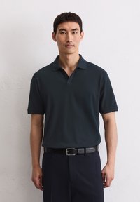 Donkerblauwe polo met V-hals en korte mouwen, met een gladde stofstructuur. Gecombineerd met donkere broeken en een zwarte riem.