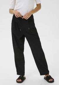 Pantalons noirs amples en tissu léger avec une taille �élastique et un cordon de serrage réglable. Portés avec des sandales noires.