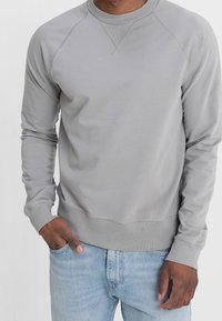 Felpa grigia con scollo rotondo, maniche lunghe, polsini e orlo a costine. Realizzata in tessuto morbido, con una vestibilità sportiva e rilassata. Design semplice.