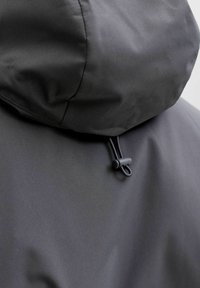 Gros plan sur la capuche d'une veste imperméable noire avec cordon de serrage réglable et embout en plastique à l'arrière.