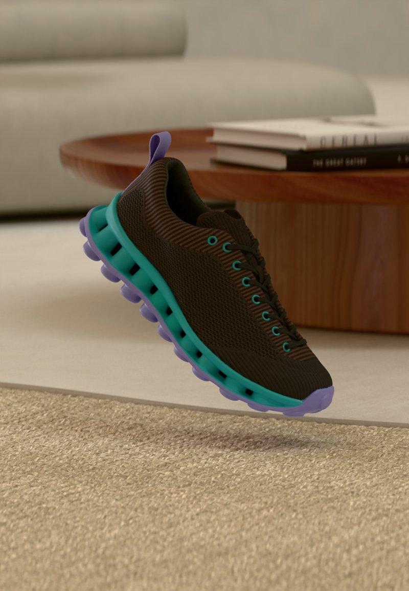 Baskets flottantes noires et marron avec une semelle turquoise et des accents violets au-dessus d'un tapis beige près d'une table basse en bois avec des livres.