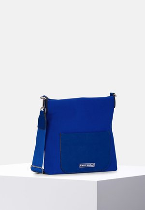 Blauwe crossbody tas met verstelbare riem en voorvak met label Emily & Noah, tentoongesteld op een witte ondergrond tegen een lichte achtergrond.