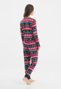 Pijamas rojos y azul marino con estampados que presentan formas geométricas, árboles y animales. Tejido suave, mangas largas y puños elásticos en los pantalones.